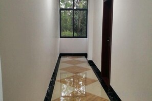 A hallway with a checkered floor pattern, a window with a view of trees, and a door on the right. - Guilin Guzhen Inn (Dawei Guzhen Inn) (Lingchuan)