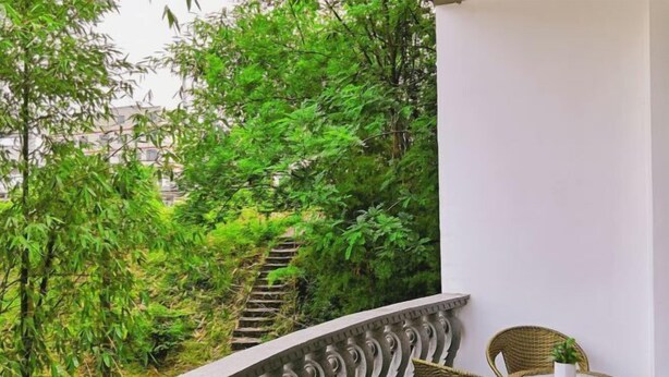 A balcony with wicker chairs and a table, surrounded by lush greenery and a staircase leading to a building. - Guilin Guzhen Inn (Dawei Guzhen Inn) (Lingchuan)