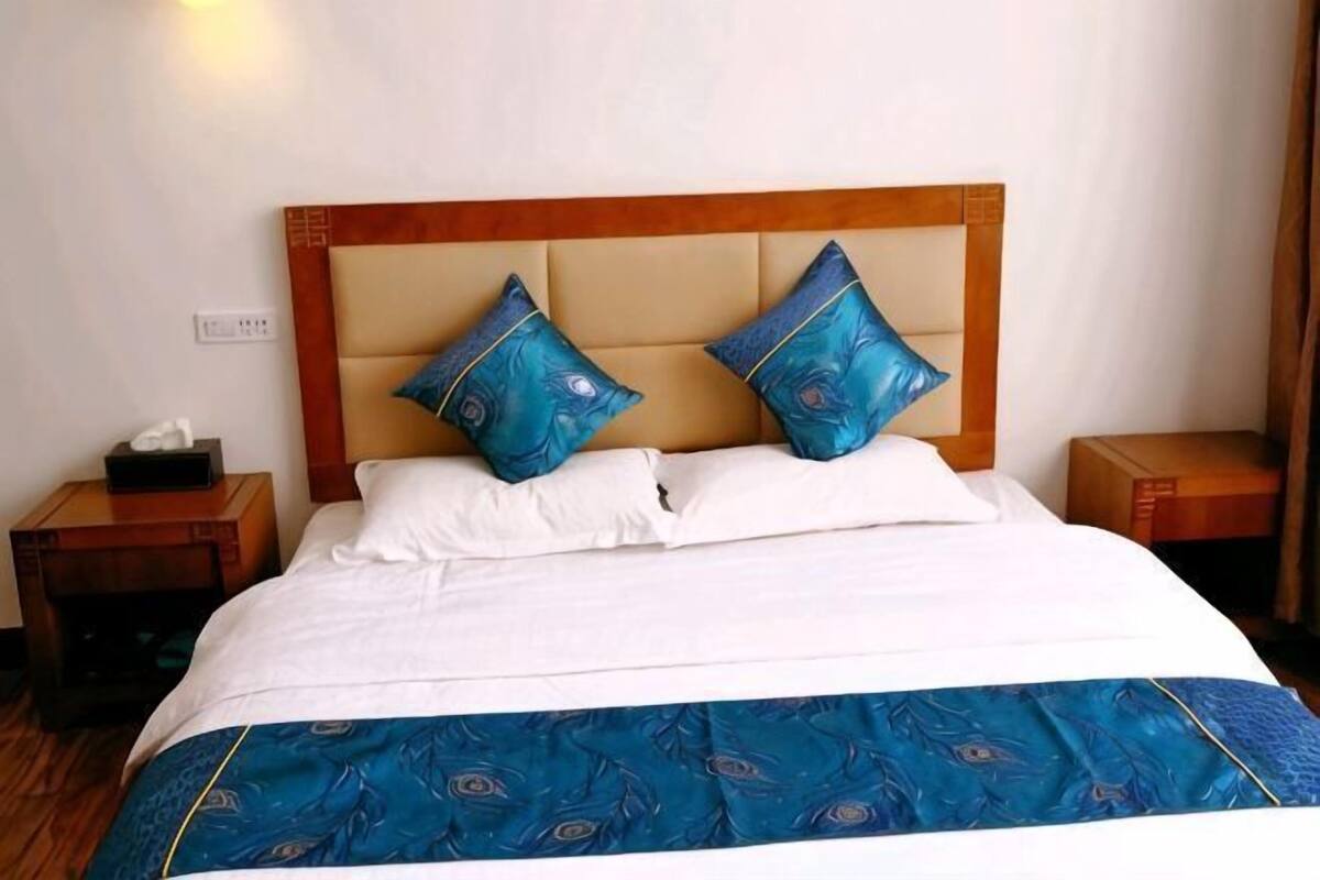 A hotel room with a bed, two pillows, a nightstand, and a bedside table.
