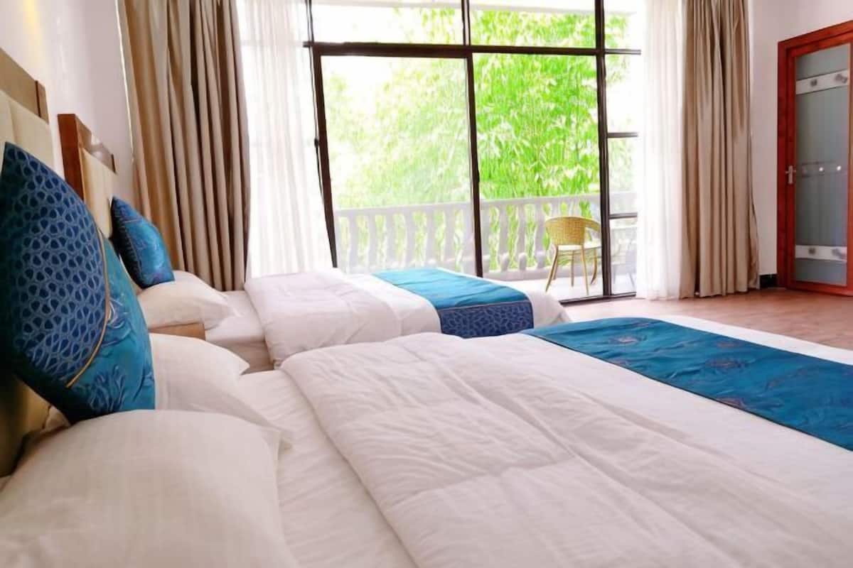 A hotel room with two beds, a large window, and a view of greenery outside.