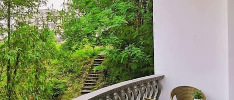 A balcony with wicker chairs, a small table, and a view of a staircase surrounded by greenery.
