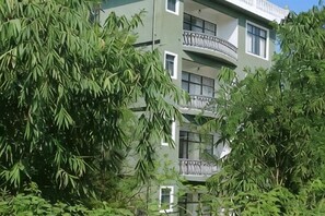 En byggnad med flera våningar och balkonger, omgiven av tät vegetation.