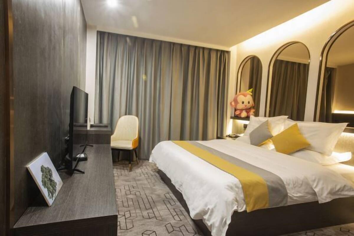 Hotellihuone, jossa on sänky, työpöytä, tuoli, televisio ja suuri peili.