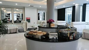 A modern hotel lobby with a central island featuring food and beverage stations, seating areas, and large windows offering views.