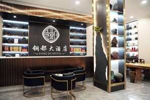 Un área de recepción de hotel con diseño moderno, que incluye un mostrador de recepción, un espacio de descanso y una exhibición de diversos objetos.