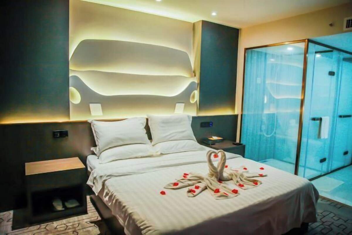 Une chambre d’hôtel moderne dotée d’un grand lit, d’un dressing fermé par des parois en verre et d’un luminaire fixé au mur.