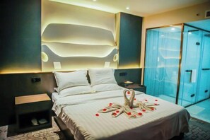Una habitación de hotel moderna con una cama grande, un vestidor con paredes de vidrio y un aplique de pared.