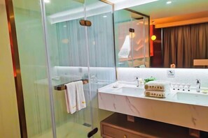 Un baño moderno con cabina de ducha de vidrio, tocador de mármol y un espejo grande.