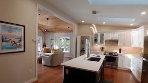 Una cocina moderna con armarios blancos, una isla central y un comedor con sofá y mesa.