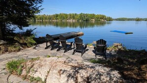 Un área de picnic junto al lago, con una mesa y sillas de piedra, rodeada de árboles y un lago tranquilo.