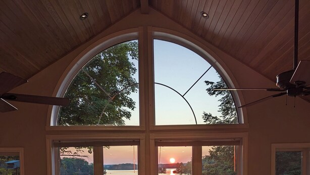 Amplia habitación con un gran ventanal de arco que da a un lago al atardecer.