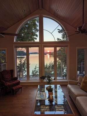 Ein geräumiger Raum mit einem großen, gewölbten Fenster mit Blick auf einen See bei Sonnenuntergang.
