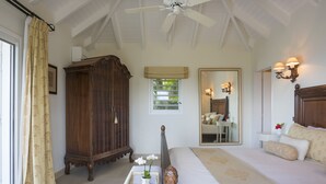 A bedroom with a large bed, a wooden cabinet, a ceiling fan, and a window with curtains.