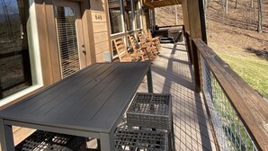 Een houten terras met een tafel en stoelen, uitkijkend op een gazon met bomen en een gebouw in de verte.