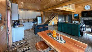 Een ruim interieur van een blokhut met keuken, eethoek en open haard.