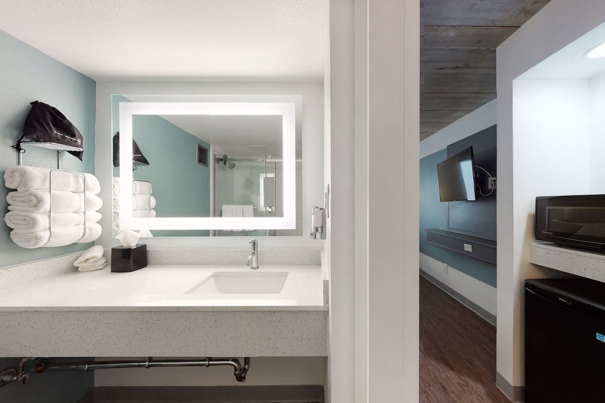 A modern bathroom with a large mirror, white sink, and towel rack.