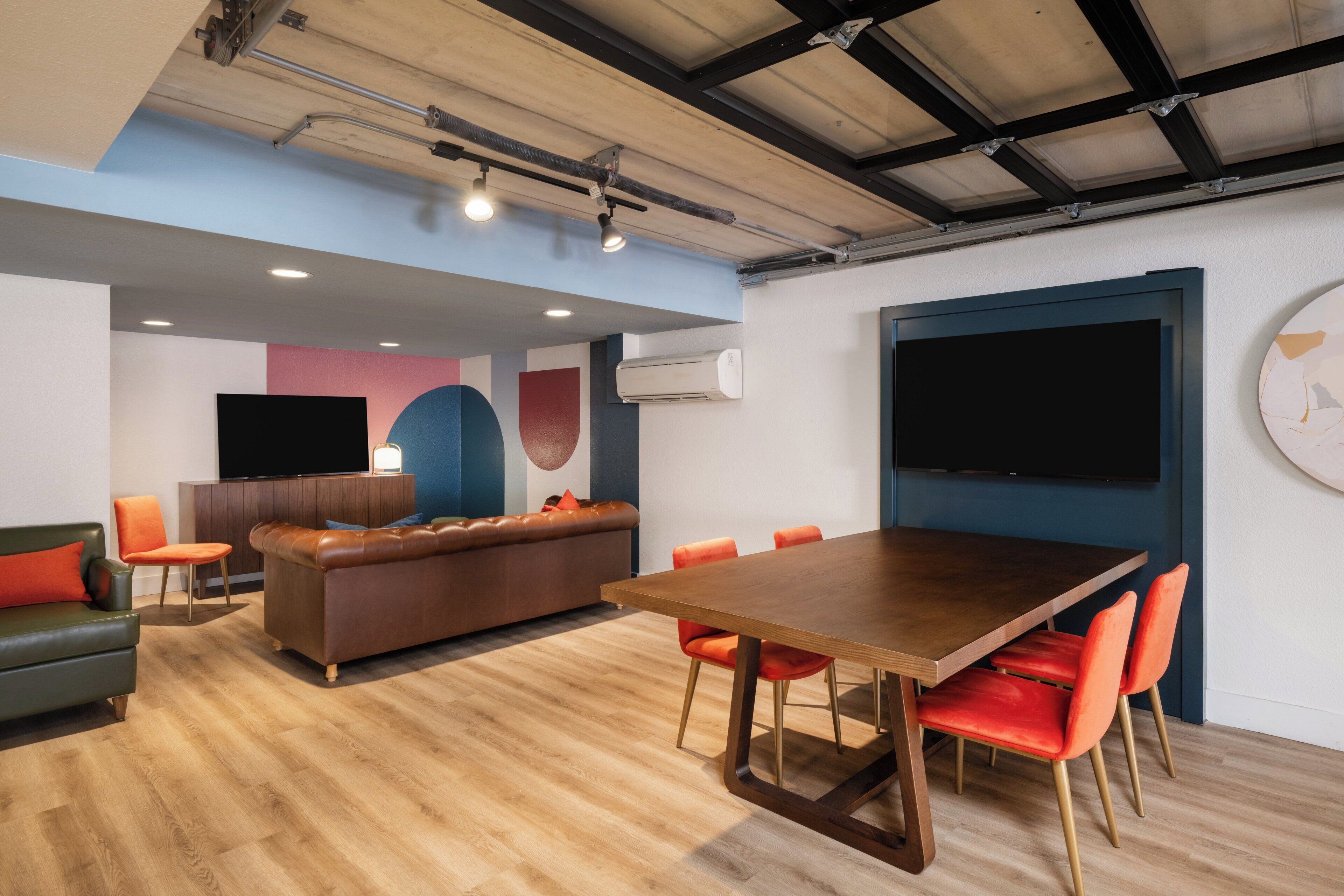 Ein moderner Konferenzraum mit einem Holztisch, roten Stühlen, einem braunen Ledersofa und einem großen Bildschirm an der Wand.