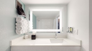 A bathroom with a white sink, a towel rack with folded towels, a tissue dispenser, and a mirror.