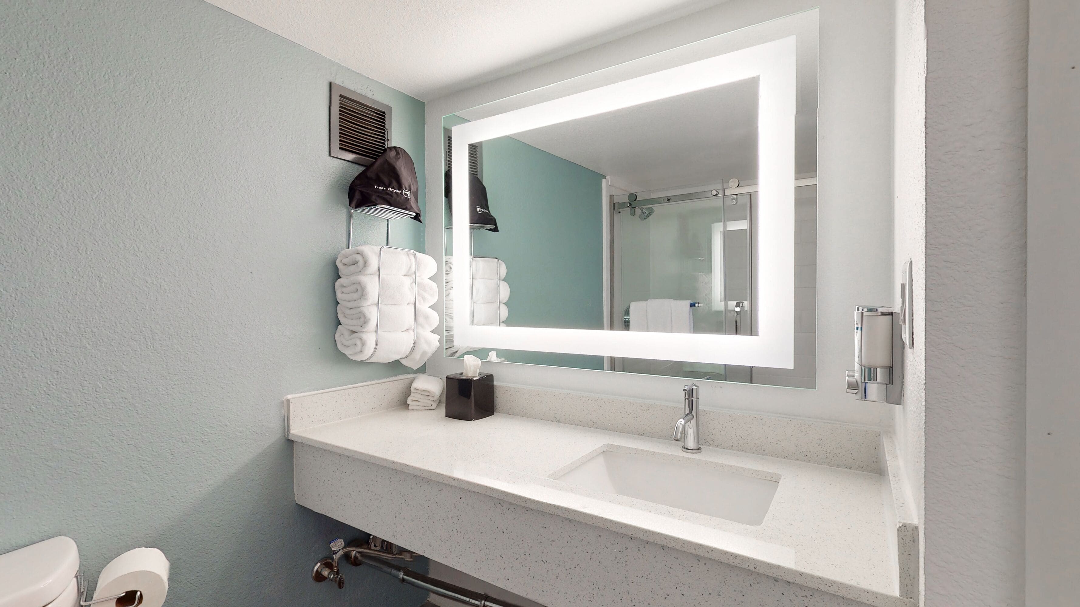 A bathroom with a white sink, a large mirror, and a towel rack with neatly folded towels.