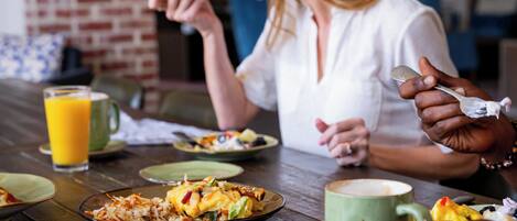 A dining table with plates of food, a glass of orange juice, and a green mug.