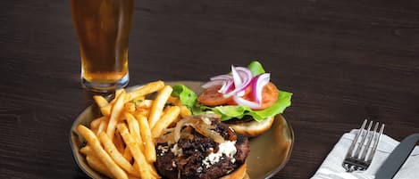 A plate with a burger, fries, and a glass of beer on a dark wooden table.