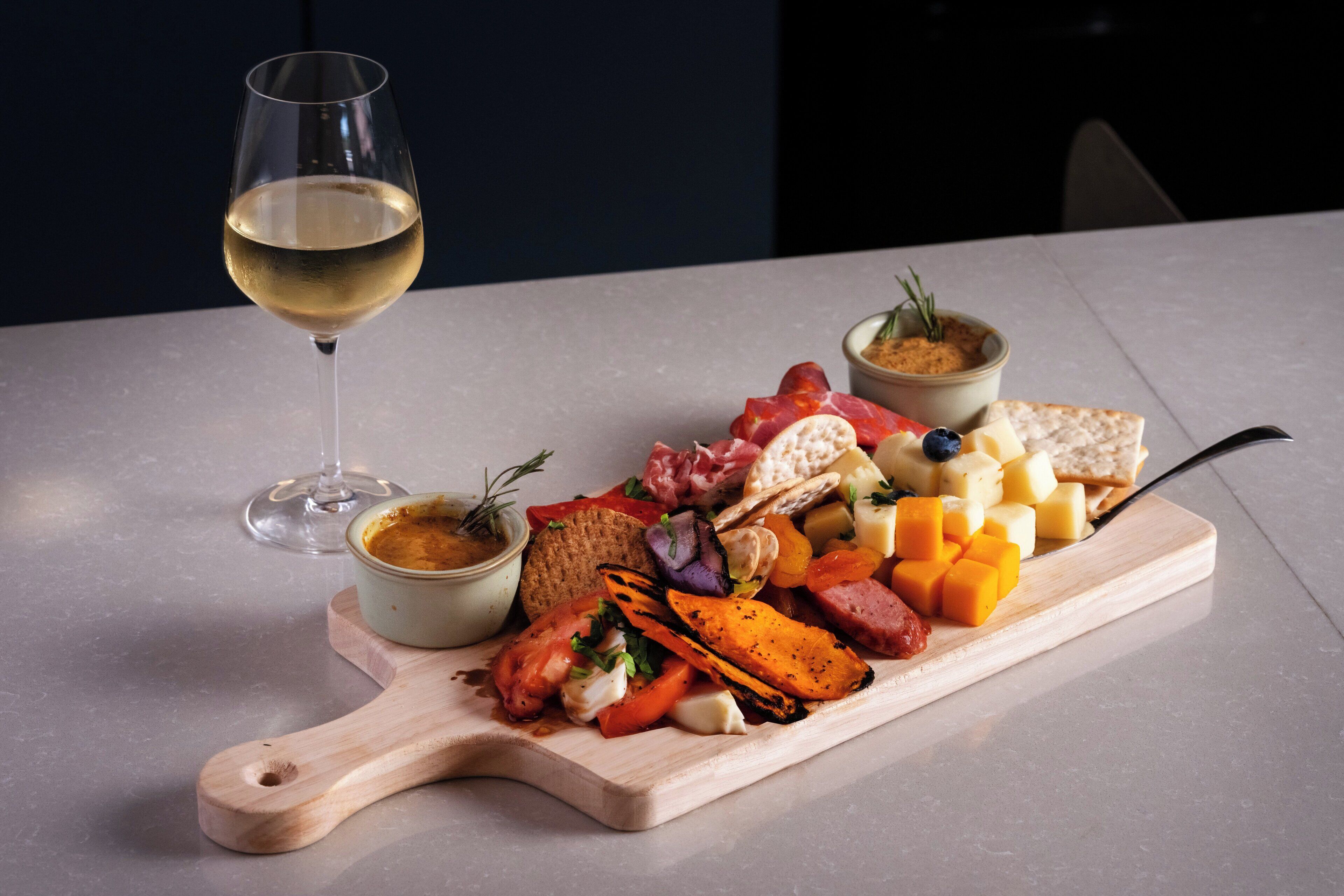 A charcuterie board with various cheeses, meats, and vegetables, accompanied by a glass of white wine on a table.
