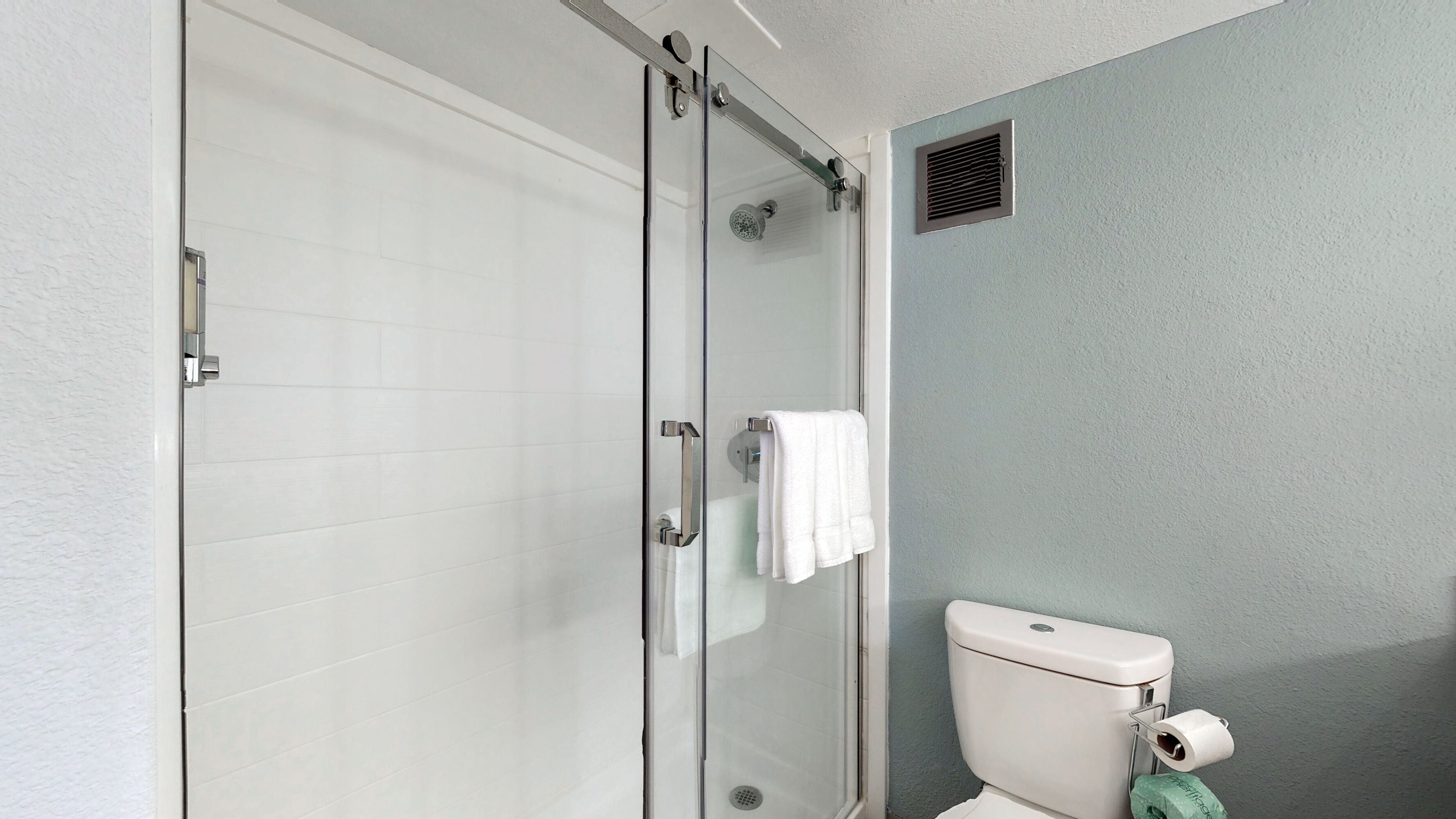 Un baño con cabina de ducha de vidrio, inodoro y perchero para toallas.