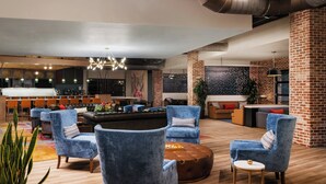 Un área de descanso moderna con sillones azules, un otoman redondo y un bar al fondo.