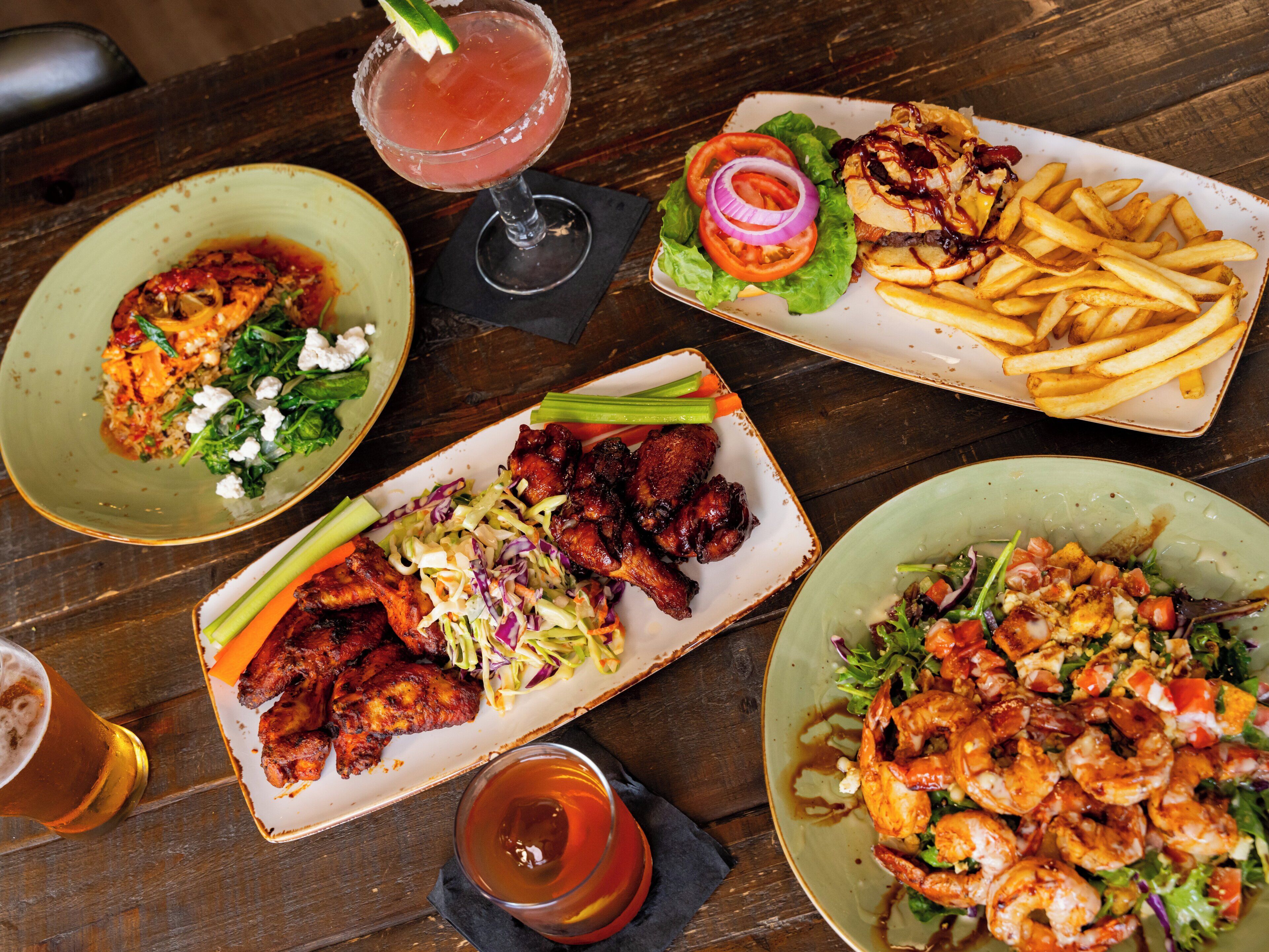 A variety of dishes including shrimp, chicken wings, and fries on a wooden table.