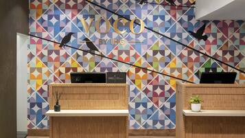 A reception area with a colorful geometric wall design, wooden reception desks, and a plant on one desk.