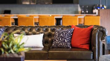 A leather sofa with patterned and solid pillows, a potted plant, and a bar area in the background.