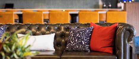 A leather sofa with patterned and solid pillows, a potted plant, and a bar area in the background.