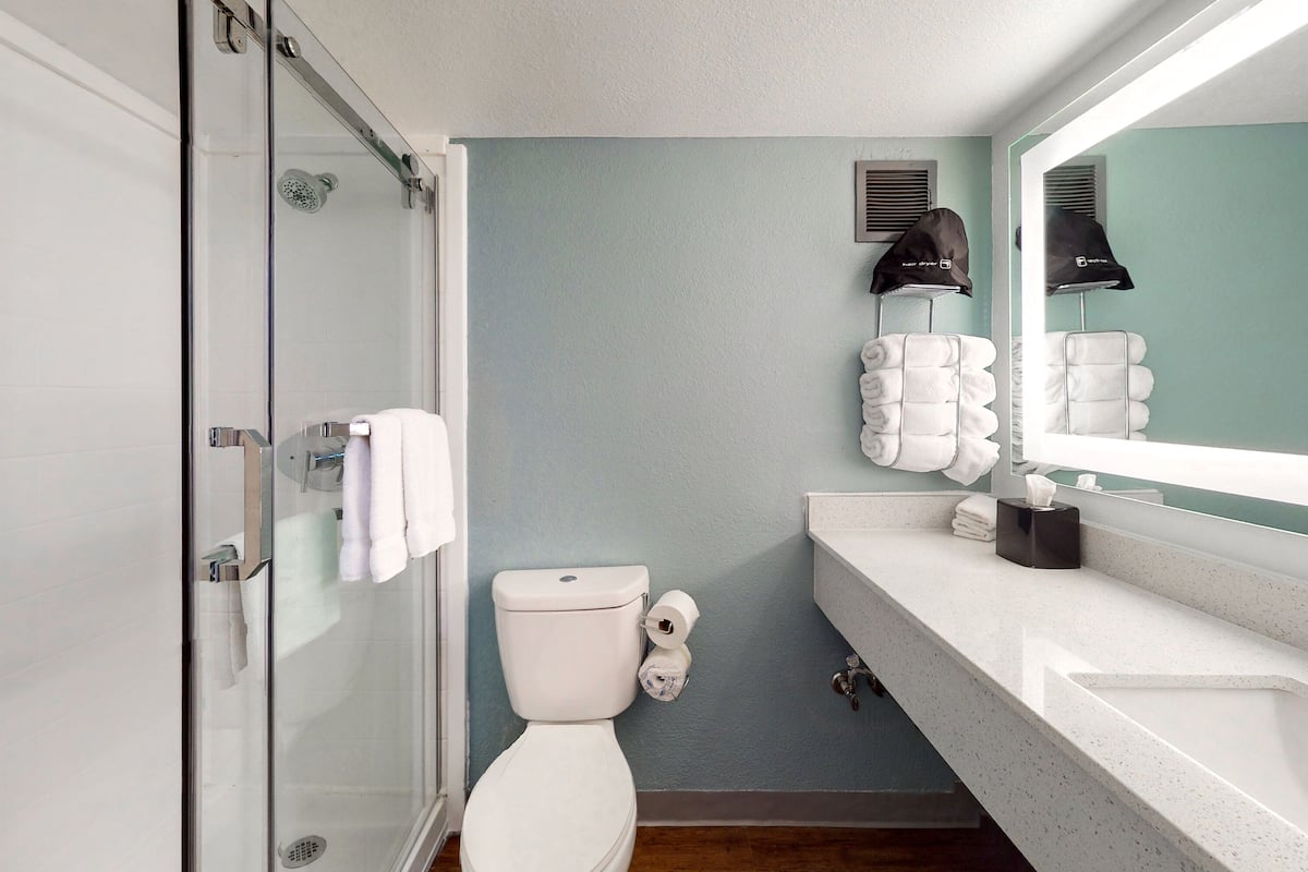A bathroom with a glass shower enclosure, a toilet, a sink with a mirror, and a towel rack with folded towels.
