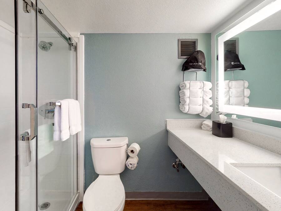 Une salle de bain avec une douche à parois de verre, des toilettes, un lavabo avec un miroir et un porte-serviettes avec des serviettes pliées.