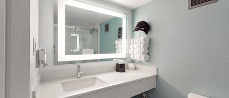 Un baño con un espejo grande, un lavamanos, un perchero para toallas y un inodoro.