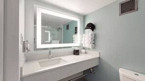 A bathroom with a large mirror, a sink, a towel rack, and a toilet.