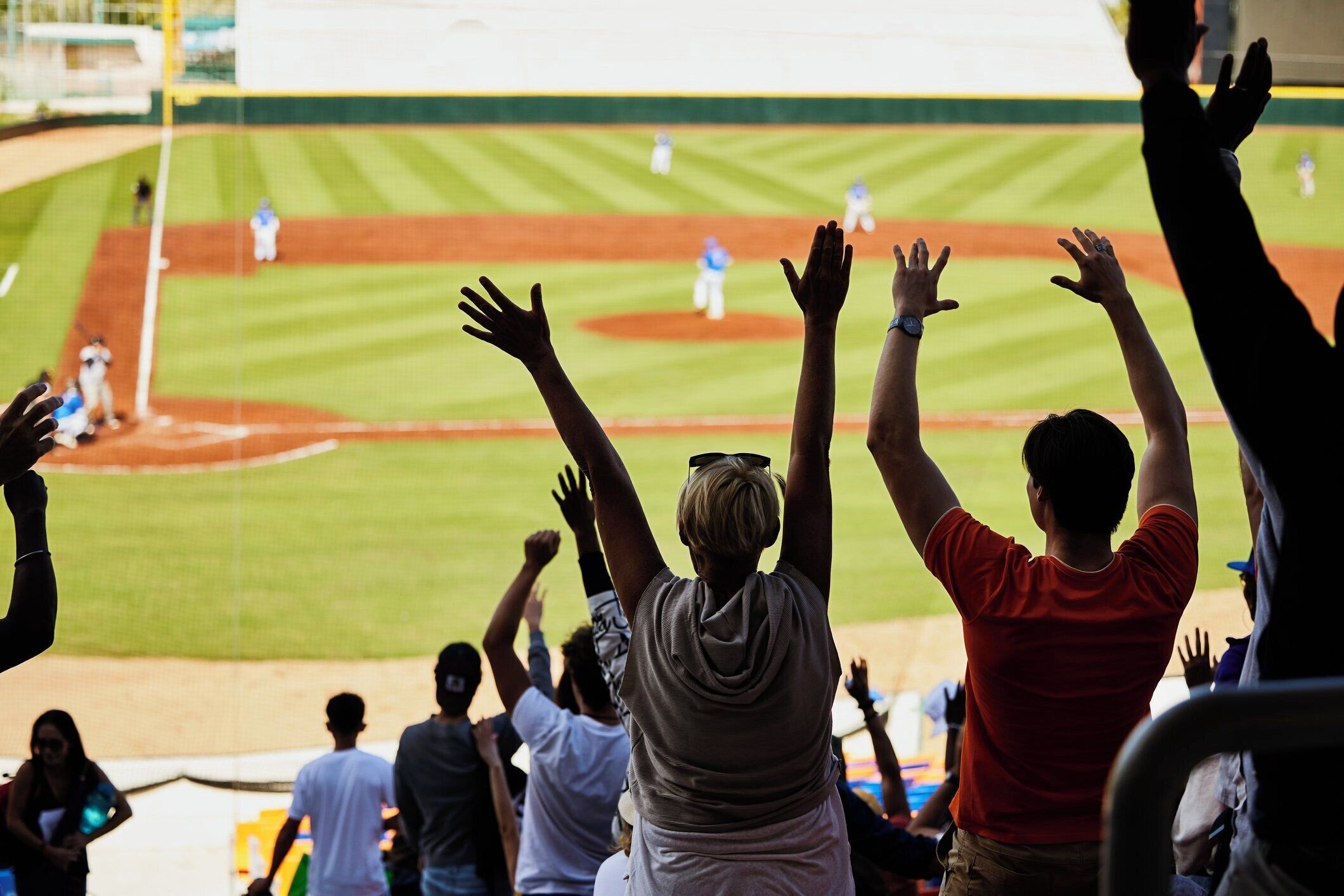 A baseball field with spectators raising their hands.