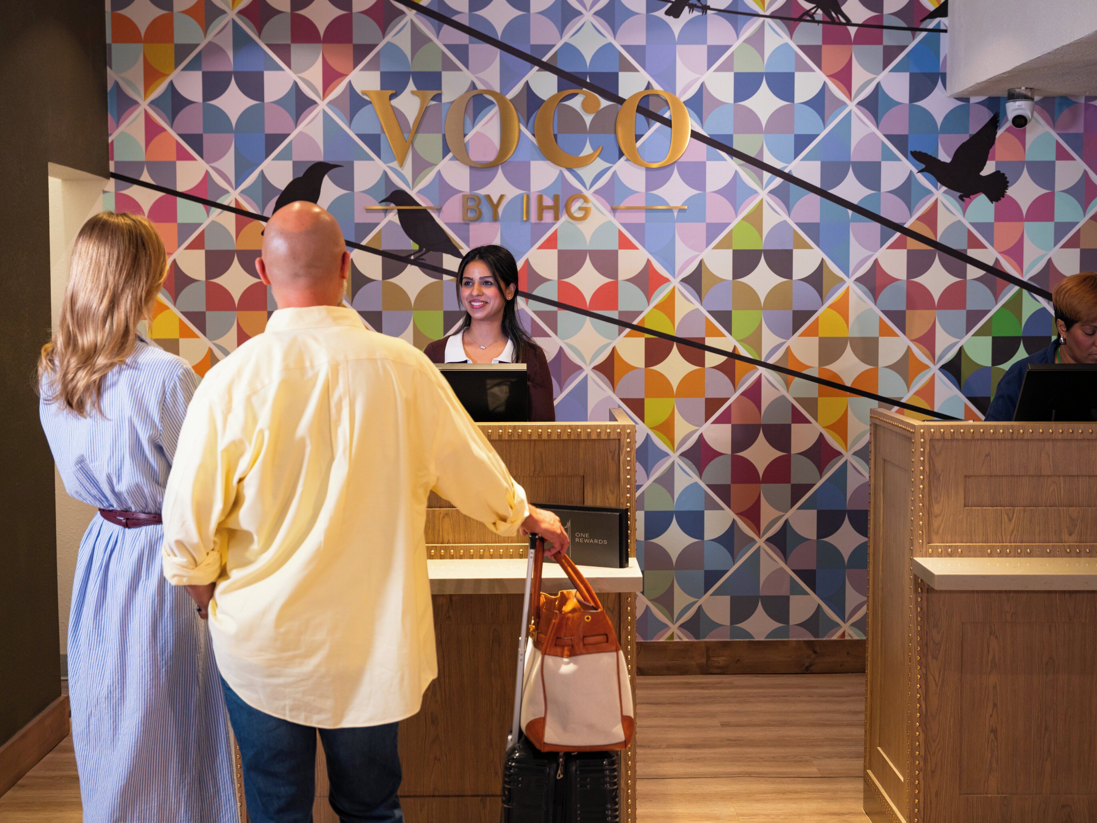 A reception area with a colorful geometric wall design, a wooden reception desk, and a woman standing behind it.