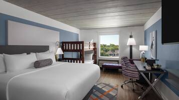 A hotel room with a large bed, a desk with a chair, a window with a view, and a lamp.