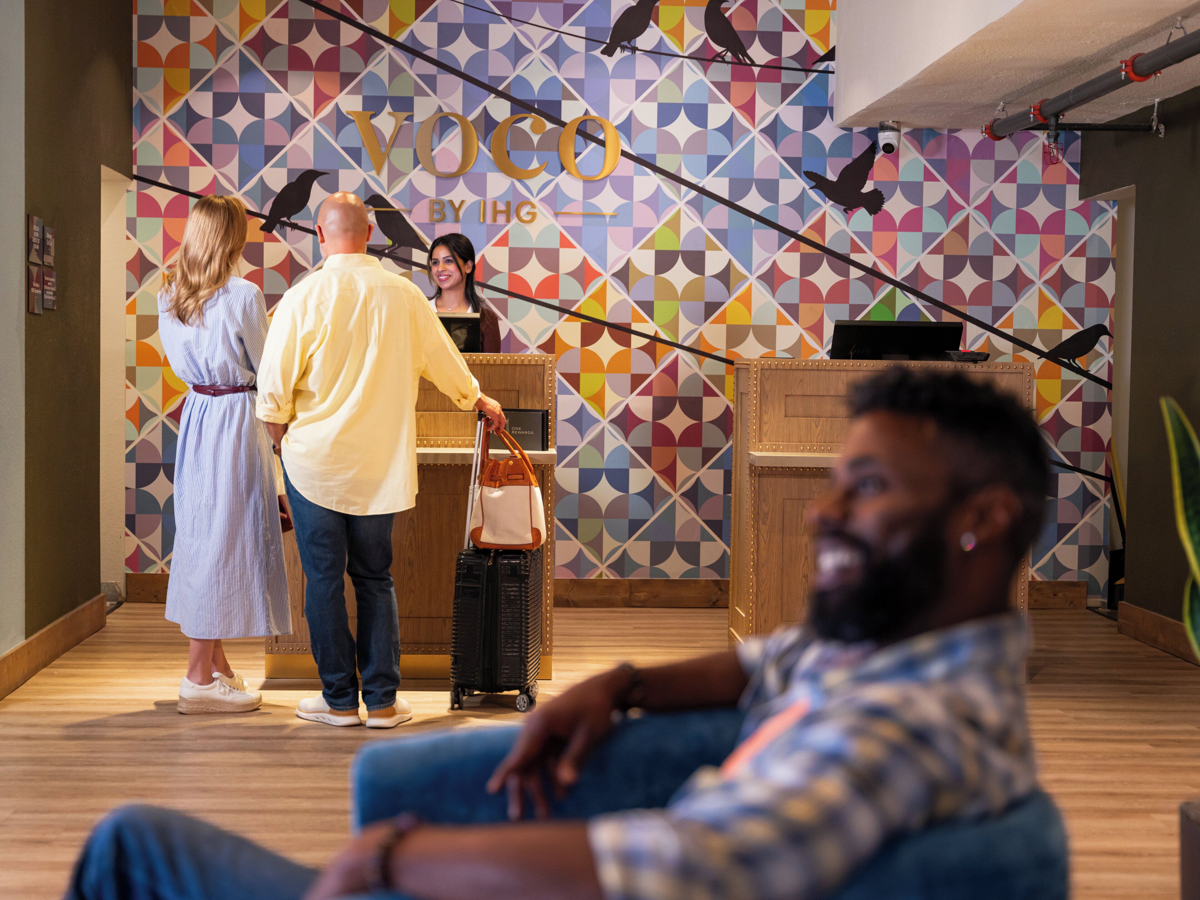 Un vestíbulo de hotel con un muro de diseño geométrico, una recepción y un área de descanso.