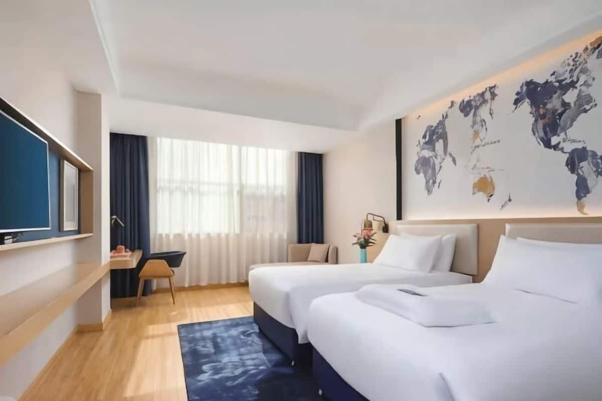 A hotel room with two beds, a desk, a chair, a TV, and a world map on the wall.