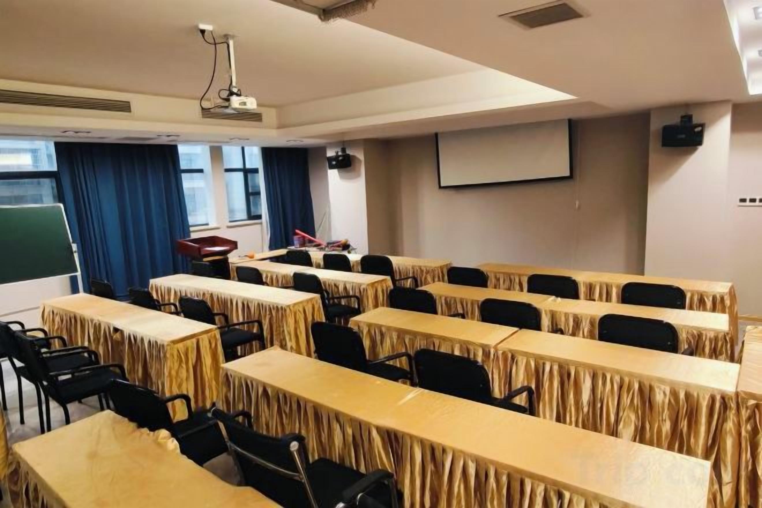 A conference room with long tables, chairs, a projector, and a screen.