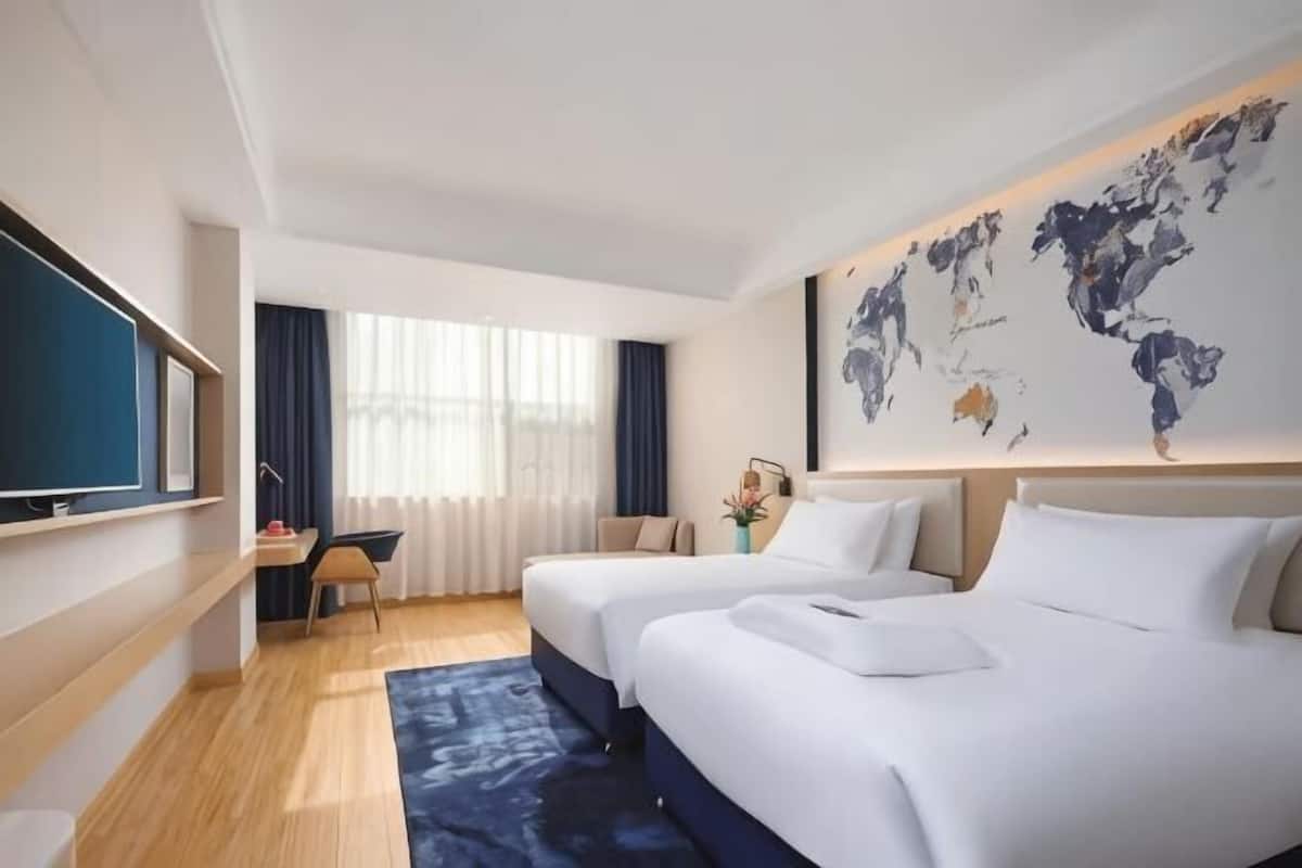 A hotel room with two beds, a desk, a TV, and a world map on the wall.
