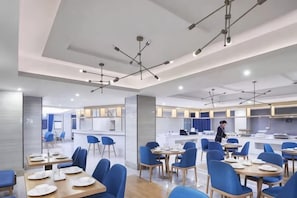 Un comedor moderno con mesas y sillas, una cocina al fondo y una persona trabajando en la barra.