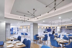 Un comedor moderno con mesas y sillas, una cocina al fondo y una persona trabajando en la barra.