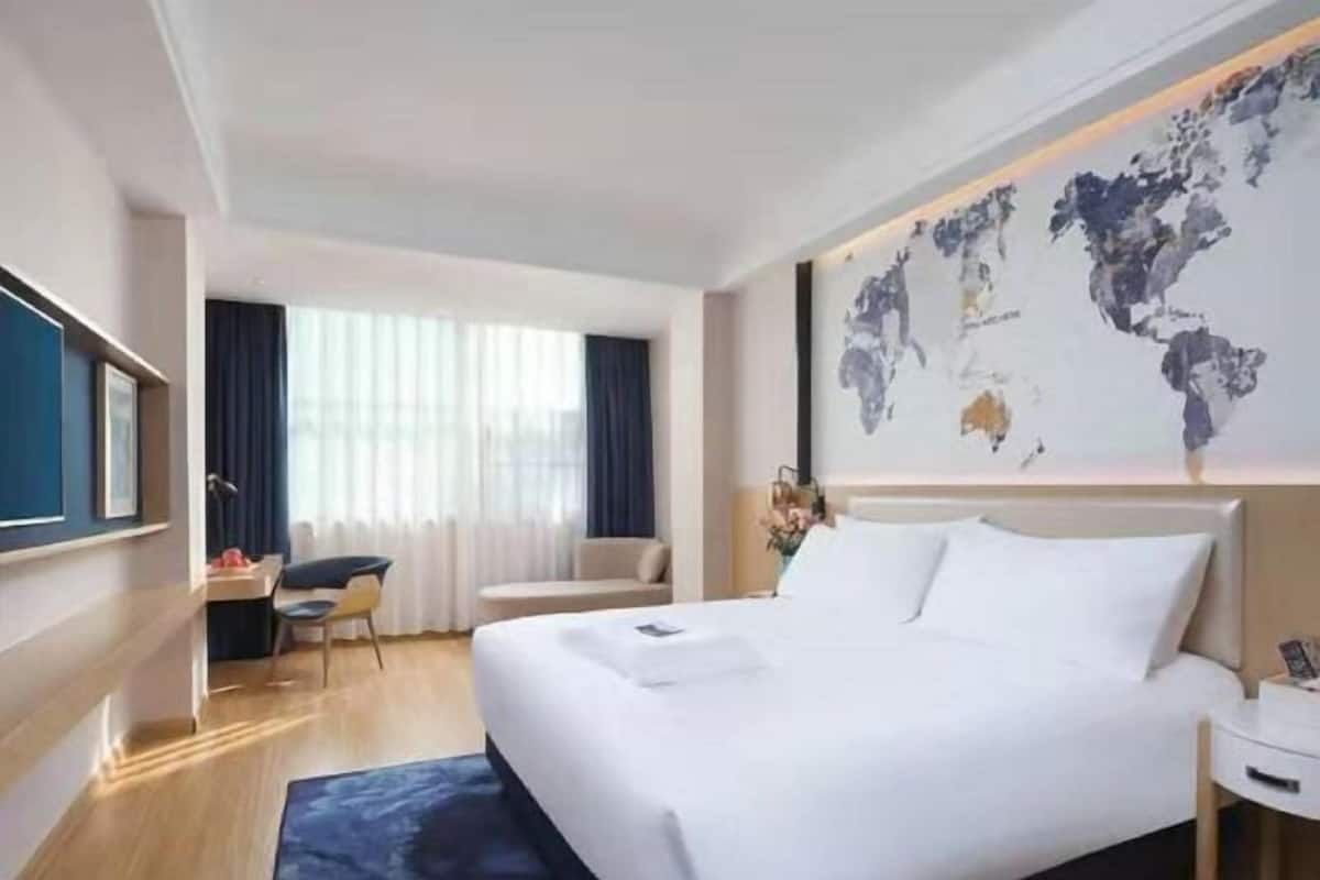 A hotel room with a large bed, a desk, a chair, and a world map on the wall.