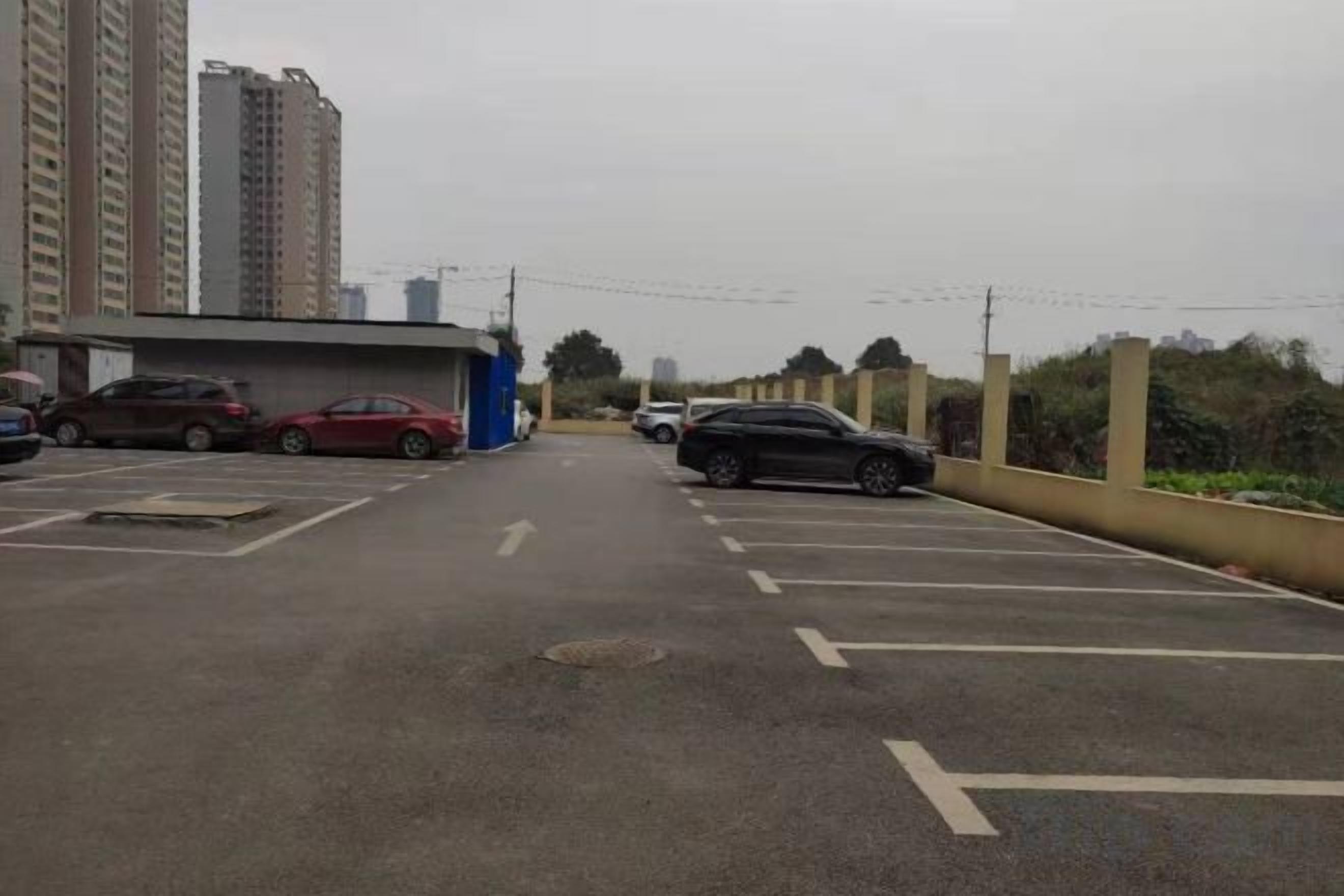 Un estacionamiento con varios autos, un edificio azul y edificios altos al fondo.