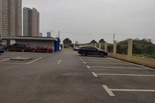 Un estacionamiento con varios autos, un edificio azul y edificios altos al fondo.