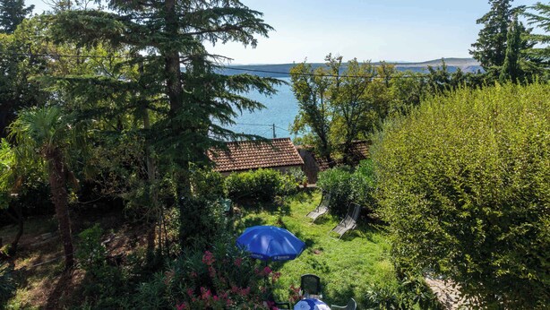 Um jardim com vista para o mar, um edifício com telhado em azulejos e área de estar ao ar livre.