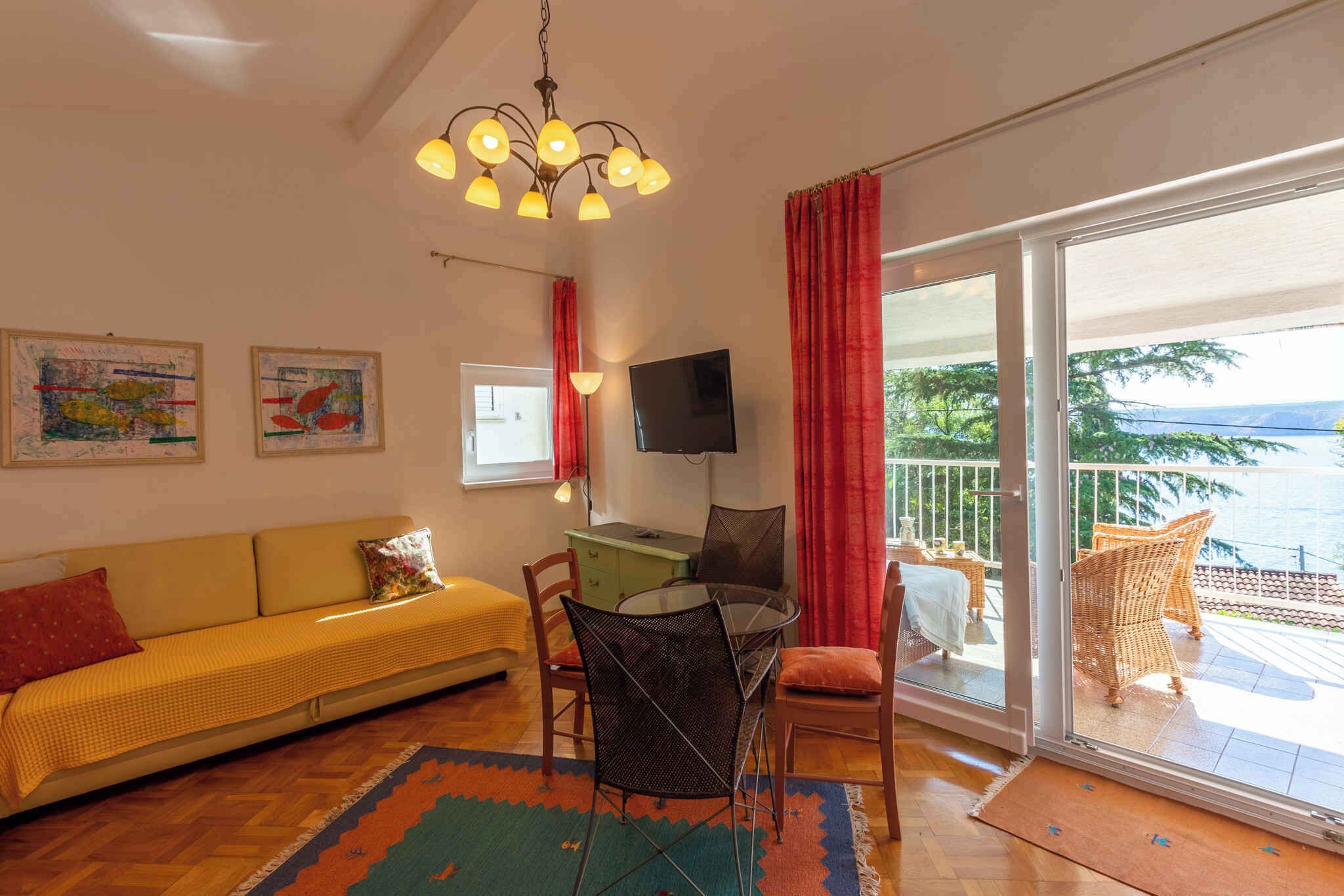 Ein Wohnzimmer mit einer Couch, einem Tisch, Stühlen, einem Fernseher und einem Balkon mit Korbmöbeln.